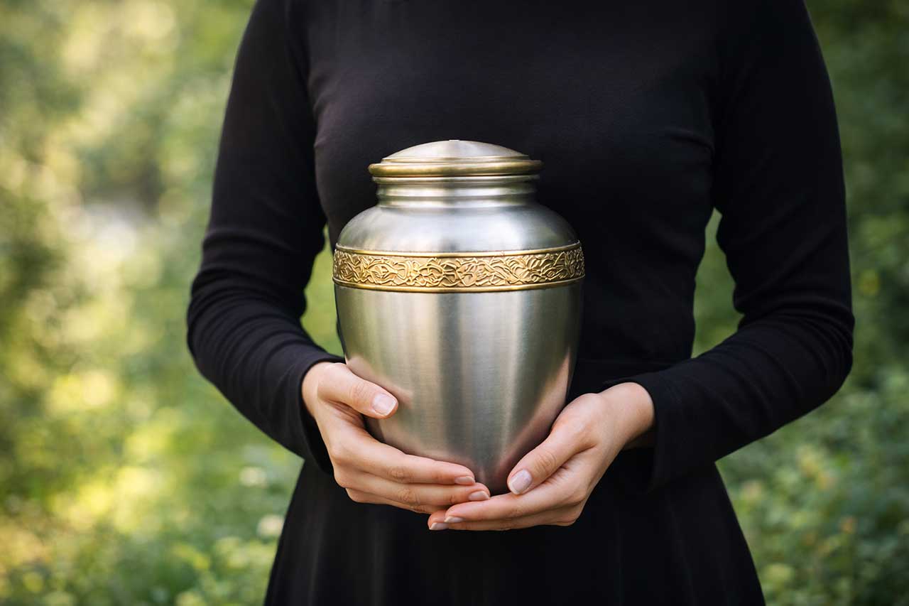 Woman In Black Dress Holding Silver Cremation Urn
